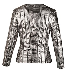 May include: Silver metallic jacket with vertical stitched detailing. The jacket has a round neckline and long sleeves. The back of the jacket is visible, showcasing the design and texture of the material. The jacket is a neutral color.
