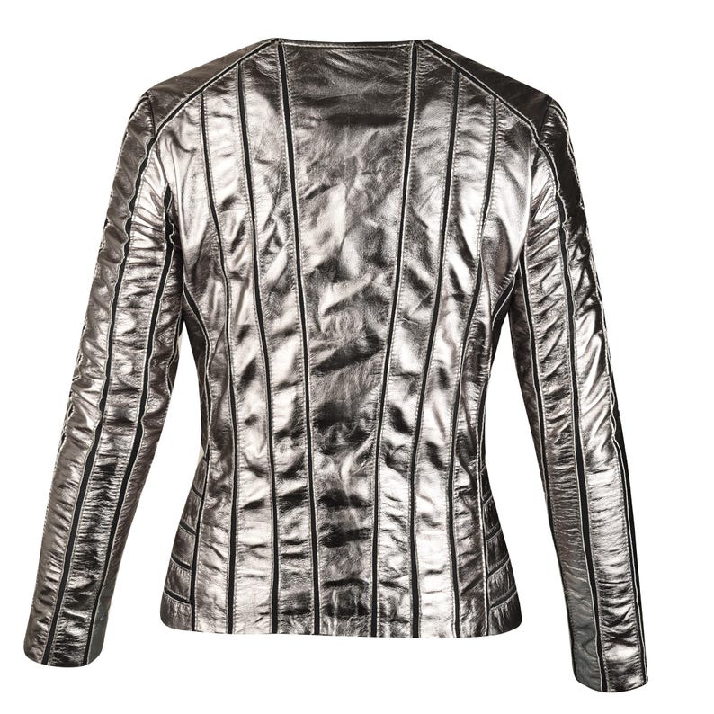 May include: Silver metallic jacket with vertical stitched detailing. The jacket has a round neckline and long sleeves. The back of the jacket is visible, showcasing the design and texture of the material. The jacket is a neutral color.