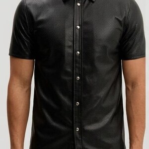 Peut inclure: Chemise noire &agrave; manches courtes avec un motif textur&eacute; et perfor&eacute;. La chemise a un col classique et une fermeture boutonn&eacute;e avec des boutons argent&eacute;s. Le v&ecirc;tement est fait d'un mat&eacute;riau brillant semblable au cuir.
