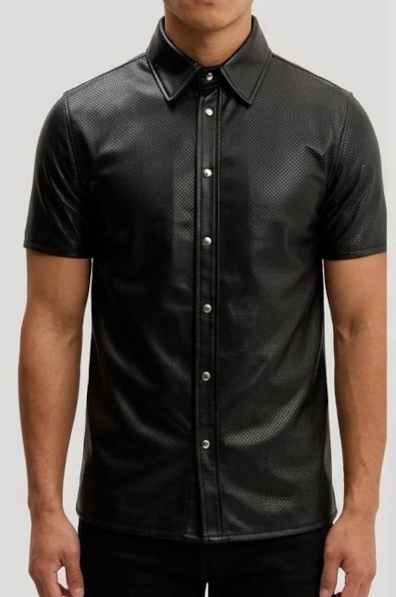 Peut inclure: Chemise noire &agrave; manches courtes avec un motif textur&eacute; et perfor&eacute;. La chemise a un col classique et une fermeture boutonn&eacute;e avec des boutons argent&eacute;s. Le v&ecirc;tement est fait d'un mat&eacute;riau brillant semblable au cuir.