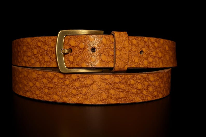 May include: A tan leather belt with a textured pattern and a brass buckle. The belt is made of a single piece of leather and has a classic design. The buckle is rectangular and has a simple, elegant look. The belt is suitable for casual or formal wear.