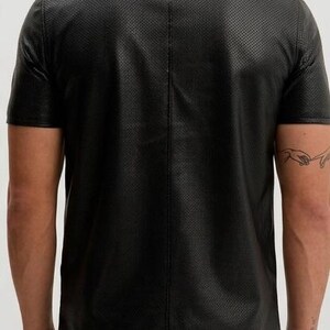 Peut inclure: Chemise noire &agrave; manches courtes avec col et motif perfor&eacute; textur&eacute;. La chemise a un design polo classique et est faite d'un mat&eacute;riau semblable au cuir. Vue arri&egrave;re de la chemise.