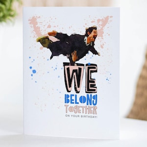 May include: A white greeting card with the words "WE BELONG TOGETHER" and a watercolor illustration of a person. The card has blue and pink paint splatters. The words "ON YOUR BIRTHDAY!" are at the bottom.