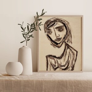 Puede incluir: Un dibujo en blanco y negro de un rostro con una expresión neutra. El dibujo está sobre un fondo beige y enmarcado en un marco de madera claro.