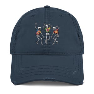 Peut inclure: Casquette de baseball bleu marine vieillie, ornée d'un motif de trois squelettes dansants portant des t-shirts tie-dye colorés. La casquette a une visière incurvée et un aspect vintage.