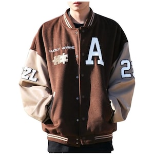 May include: A brown and tan varsity jacket with the letter "A" and the number "2" in white. The jacket has the words "LUCKY ARRIVE" and a puzzle piece design. The jacket has a button-up front and pockets.