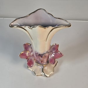 May include: A ceramic vase with an iridescent cream finish and a flared, wavy rim. The base features three-dimensional sculpted flowers in shades of pink and purple, with delicate gold trim accenting the edges of the petals and the vase rim.