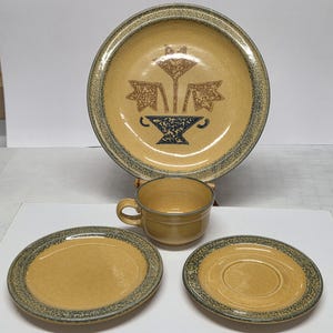 May include: A vintage ceramic dinnerware set in a warm yellow hue with a speckled blue-gray trim. The set includes a large plate with a floral design, a cup, a saucer, and a smaller plate. The floral design features brown and blue accents.