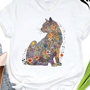 May include: White t-shirt featuring a seated cat design filled with colorful flowers. The cat illustration includes shades of purple, orange, yellow, and green. The shirt has short sleeves and a round neckline. The Southern Mama US logo is visible in the upper right corner.