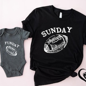 Puede incluir: Una camiseta negra con la palabra "SUNDAY" y un gr&aacute;fico de f&uacute;tbol americano. Un body gris para beb&eacute; con la palabra "FUNDAY" y un gr&aacute;fico de f&uacute;tbol americano. Ambas camisetas son blancas sobre un fondo rosa claro.