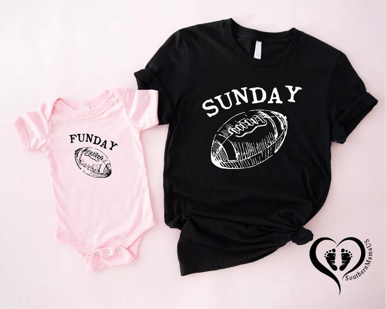 Puede incluir: Una camiseta negra con la palabra "SUNDAY" y un gr&aacute;fico de f&uacute;tbol americano, junto a un body rosa para beb&eacute; con la palabra "FUNDAY" y un gr&aacute;fico de f&uacute;tbol americano a juego. Fondo rosa claro.