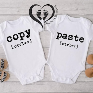 May include: Two white baby onesies with the words "copy" and "paste" printed in black, along with their respective keyboard shortcuts. The image includes a pair of baby shoes and a heart-shaped design with footprints.