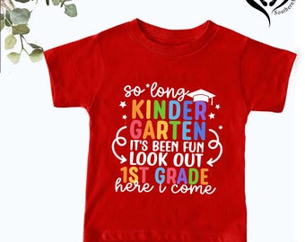 Puede incluir: Una camiseta roja con la frase "so long KINDERGARTEN, IT'S BEEN FUN, LOOK OUT 1ST GRADE, here i come" en letras coloridas. La camiseta tiene un gorro de graduación y estrellas, ideal para el paso a primero de primaria.
