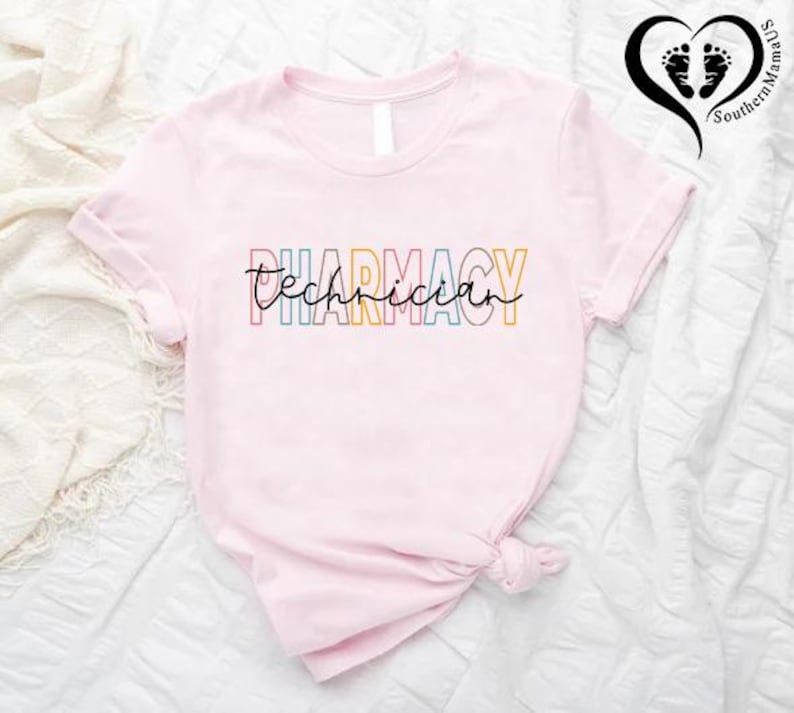 K&ouml;nnte beinhalten: Hellrosa T-Shirt mit dem Aufdruck "Pharmacy Technician" in bunten Buchstaben. Das Wort "Pharmacy" ist in verschiedenen Farben geschrieben. Das T-Shirt ist am unteren Ende geknotet.
