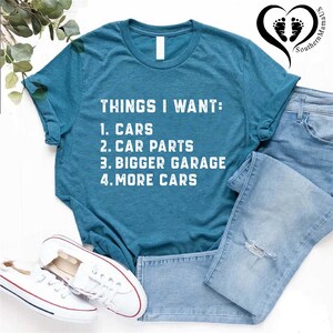Puede incluir: Una camiseta azul turquesa con texto blanco que dice "THINGS I WANT: 1. CARS 2. CAR PARTS 3. BIGGER GARAGE 4. MORE CARS".