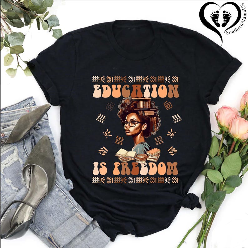 Puede incluir: Camiseta negra con el texto "EDUCATION IS FREEDOM" en letras marrones y naranjas. El gr&aacute;fico presenta a una mujer con gafas y libros en la cabeza. La camiseta se combina con vaqueros azules y zapatos grises.