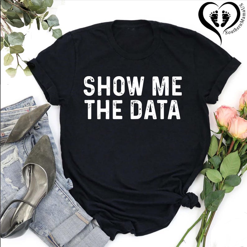 May include: Black t-shirt with the white text "SHOW ME THE DATA". The shirt is styled with a pair of blue jeans, gray heels, and a bouquet of pink roses. The Southern MamaUS logo is in the upper right corner.