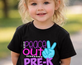 Puede incluir: Un niño lleva una camiseta negra con las palabras "peace out PRE-K" en rosa, azul y morado. El diseño incluye un signo de la paz y lunares. El niño está sonriendo.