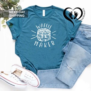 Puede incluir: Camiseta de color turquesa con un gr&aacute;fico blanco de una m&aacute;quina para hacer gofres y el texto "WAFFLE MAKER". La camiseta se combina con vaqueros azul claro y zapatillas blancas. La imagen tambi&eacute;n incluye el texto "NEXT DAY SHIPPING".