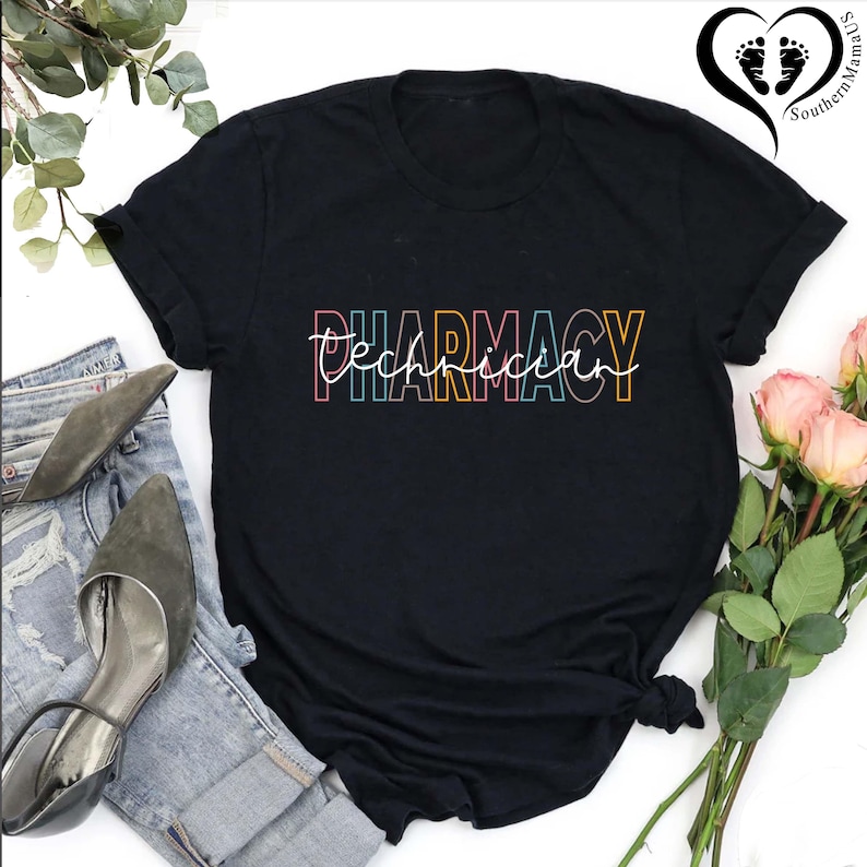 K&ouml;nnte beinhalten: Schwarzes T-Shirt mit dem Schriftzug "Pharmacy Technician" in einer farbenfrohen, umrandeten Schriftart. Der Text ist eine Mischung aus Block- und Schreibschrift. Das Shirt wird mit Jeans, Abs&auml;tzen und Blumen gezeigt.
