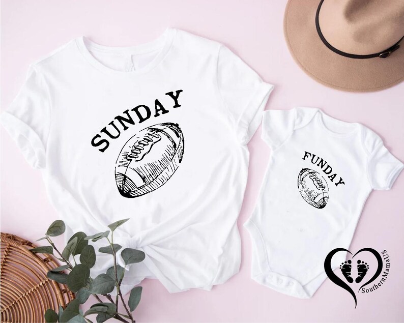 Puede incluir: Camiseta blanca con la palabra "SUNDAY" encima de un gr&aacute;fico de f&uacute;tbol americano. Un body de beb&eacute; blanco a juego con la palabra "FUNDAY" y un gr&aacute;fico de f&uacute;tbol americano. Un sombrero marr&oacute;n en el fondo.