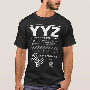 May include: Black t-shirt with a white graphic design of the Toronto Pearson International Airport (YYZ) code, coordinates, and runway information. The text reads "YYZ - Toronto, ONT. CANADA, N43°40.63/W79°3133, 569 FT./173 M MSL, VARIATION: 19%, LESTER B. PEARSON INTL, RWYS 05-23, 15L-338, OGL-248, 15R-33L, 06R-24L".