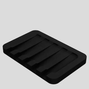 Könnte beinhalten: Schwarze rechteckige Seifenschale mit erhöhten Rippen zur Entwässerung. Die Schale besteht aus einem gummiartigen Material.