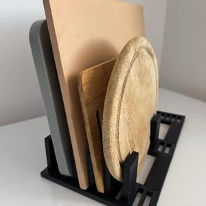 Könnte beinhalten: Ein schwarzer Küchenorganizer aus Kunststoff, der vier Gegenstände hält: ein graues rechteckiges Tablett, ein großes rechteckiges beiges Steinbrett, ein rechteckiges Holzschneidebrett und ein rundes Holzschneidebrett mit Rille.