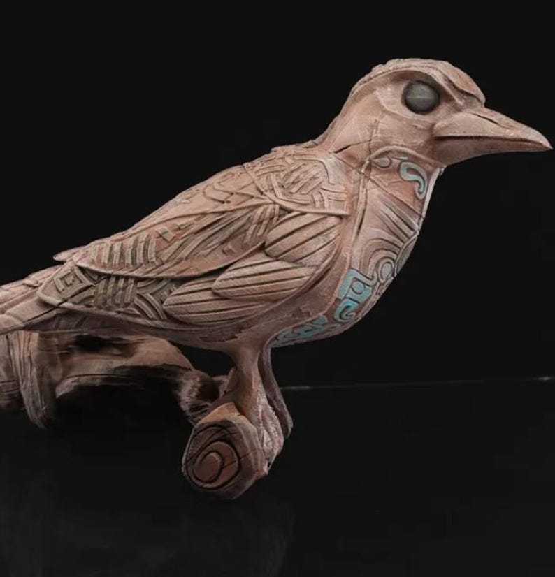 May include: A detailed, intricately carved wooden bird sculpture with a light brown finish. The bird is perched on a branch and has a stylized design with geometric patterns.