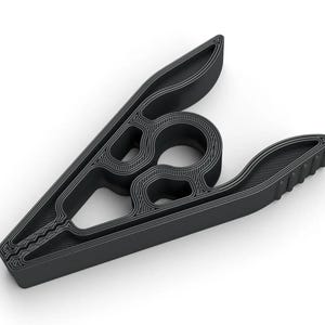 May include: A black plastic clothes hanger with a unique, layered design. The hanger features a central circular element and two curved arms with textured edges. The overall shape is reminiscent of a stylized clamp.