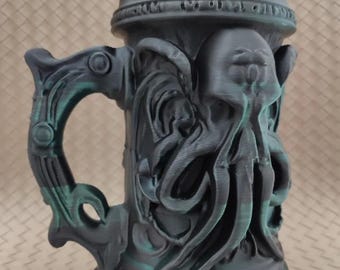 May include: A dark gray beer stein with an octopus design. The stein has a handle and a lid, and the design includes tentacles and other sea creature elements. The top of the stein holds a white can with text.