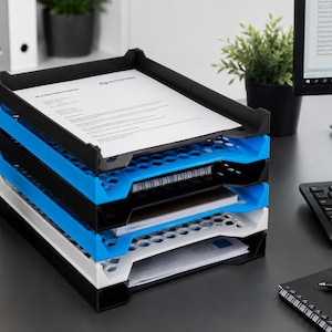May include: A stackable desk organizer with four trays in black, blue, and white. The trays are filled with papers and documents. A black pen holder with pens and a computer keyboard are also visible.