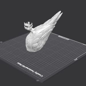 May include: A white 3D printed sculpture of a bird with its wings spread out. The sculpture is on a gray textured bed.