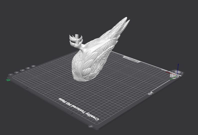 May include: A white 3D printed sculpture of a bird with its wings spread out. The sculpture is on a gray textured bed.