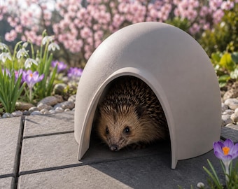 May include: A hedgehog peeks out from a light gray, dome-shaped shelter. The shelter is on a gray stone patio, surrounded by spring flowers, including purple crocuses and white snowdrops. The hedgehog has brown and tan quills.