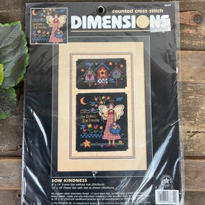 Puede incluir: Un kit de punto de cruz contado Dimensions titulado "Sow Kindness". El kit incluye un diseño enmarcado con un ángel, flores y casitas para pájaros. El kit está empaquetado en una funda de plástico transparente. El tamaño del marco sin paspartú es de 20x36cm.