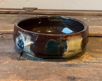 Könnte beinhalten: Eine braune Keramikschüssel mit weißer und blauer Glasur. Die Schüssel hat eine leicht unregelmäßige Form und steht auf einer Holzoberfläche.