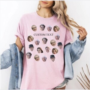 May include: A light pink t-shirt featuring a collection of faces arranged in a pattern. The shirt has the words "CUSTOM TEXT" printed on it. The shirt is a casual style.