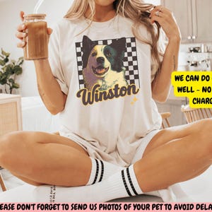 May include: Cream-colored t-shirt featuring a graphic of a dog named Winston, set against a checkered background. The text "Winston" is in a stylized font. The shirt also has the text "WE CAN DO CATS AS WELL - NO EXTRA CHARGE".