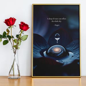 May include: A framed art print with a gold border features a surreal image of a water droplet reflecting a galaxy. The print includes the quote "A drop of water can reflect the whole sky." Two red roses in a clear vase are on the left.