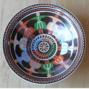 Könnte beinhalten: Ein runder Keramikteller mit braunem Hintergrund und einem farbenfrohen Design von Figuren, die sich in einem Kreis an den Händen halten. Die Figuren sind in Rot-, Orange-, Grün-, Blau- und Weißtönen bemalt.