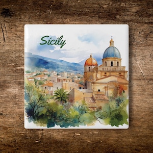 May include: A square ceramic tile featuring a watercolor painting of a Sicilian townscape. The image includes buildings, a church with a blue dome, and the word "Sicily" in green script. The artwork is set against a backdrop of mountains and greenery.