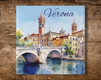 May include: A square ceramic tile featuring a watercolor illustration of the city of Verona, Italy. The image depicts a stone bridge over a river with historic buildings and towers in the background. The word Verona is printed in blue script.