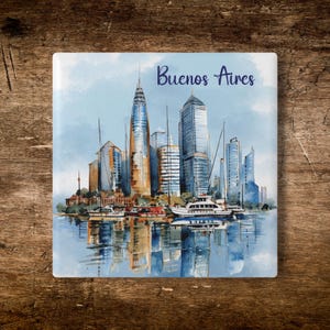 Puede incluir: Posavasos cuadrado con una pintura de acuarela del horizonte de Buenos Aires, barcos en el agua y el nombre de la ciudad en escritura azul. La imagen tiene una combinación de colores azul claro y blanco.