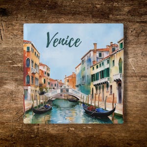 May include: A square decorative tile featuring a watercolor-style illustration of a Venice canal scene with the word Venice printed in dark script. The image displays colorful buildings, a stone bridge, and two black gondolas on the water.