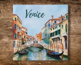 May include: A square decorative tile featuring a watercolor-style illustration of a Venice canal scene with the word Venice printed in dark script. The image displays colorful buildings, a stone bridge, and two black gondolas on the water.