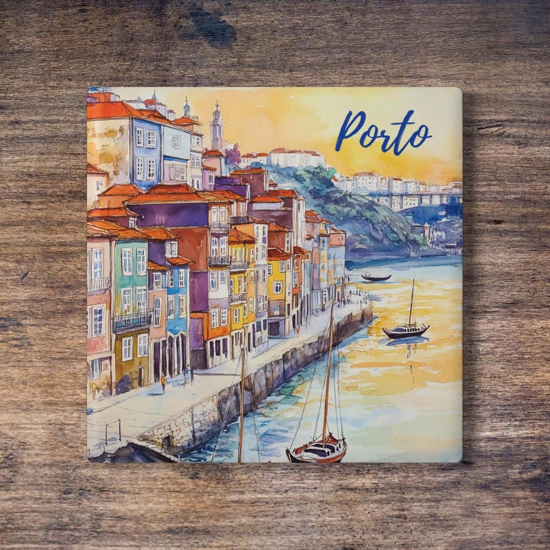 May include: Square watercolor print of Porto, Portugal, featuring colorful buildings with orange rooftops along a river. The word "Porto" is written in blue script. Several sailboats are on the water, and the background shows a bridge and a hillside.