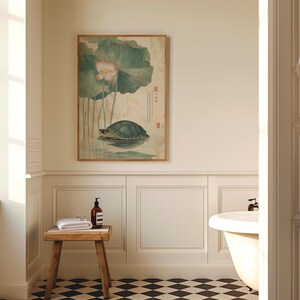May include: A bathroom scene featuring a framed artwork of a turtle in water with a lotus flower. A small wooden stool holds a rolled white towel and a brown bottle. The room has white paneling, a black and white checkered floor, and a white bathtub.