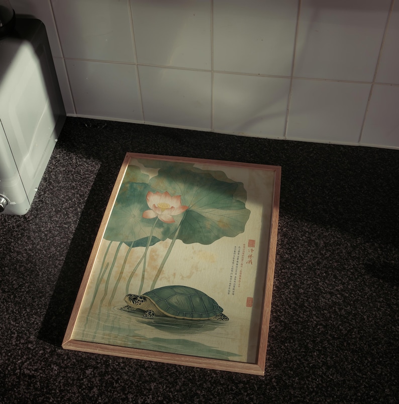 May include: A framed artwork featuring a turtle in water beneath a lotus flower and large leaves. The artwork has a light wood frame and a traditional Asian painting style with soft colors.