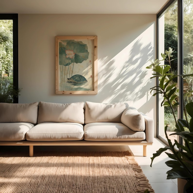 May include: A beige sofa with a wooden frame and legs sits on a woven rug. A framed artwork depicting a turtle and lotus flowers hangs on the wall. The room has a neutral color palette with natural light.